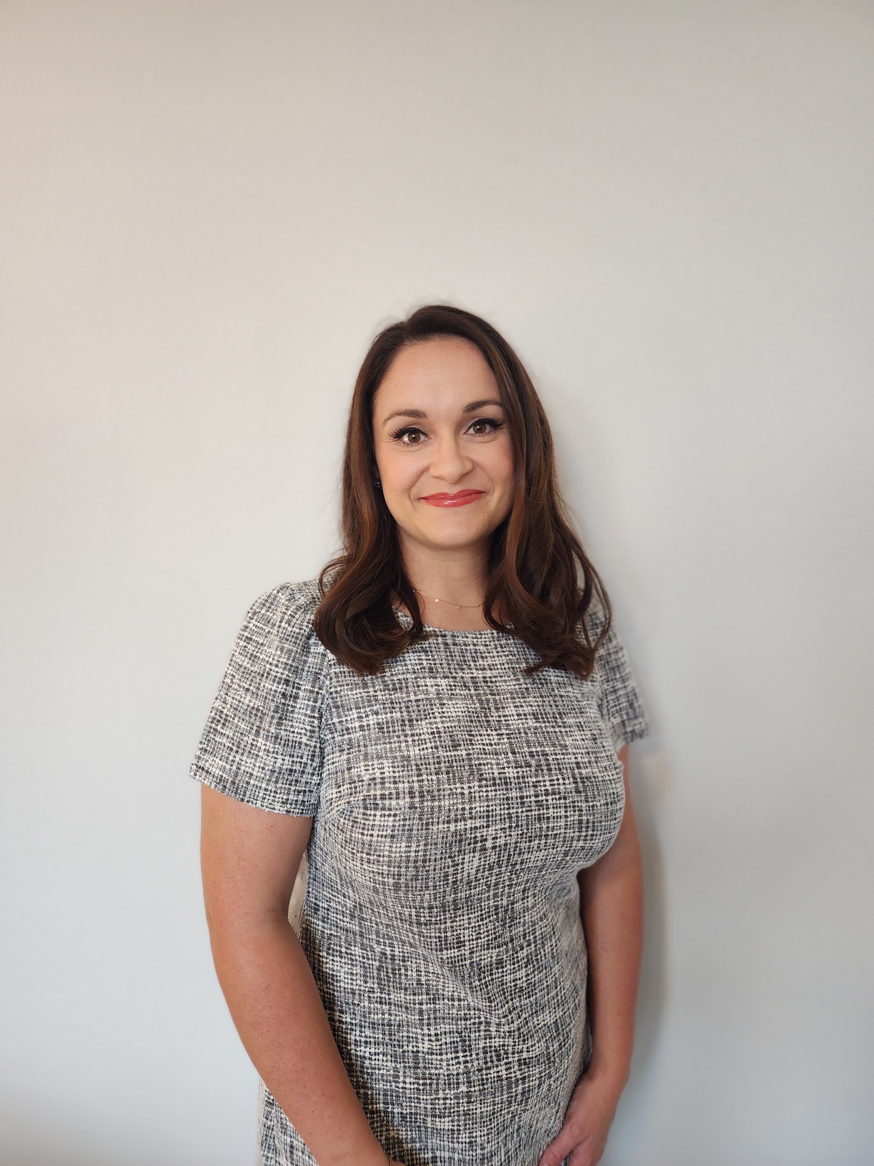 A smiling woman with long brown hair in a textured gray and white dress.